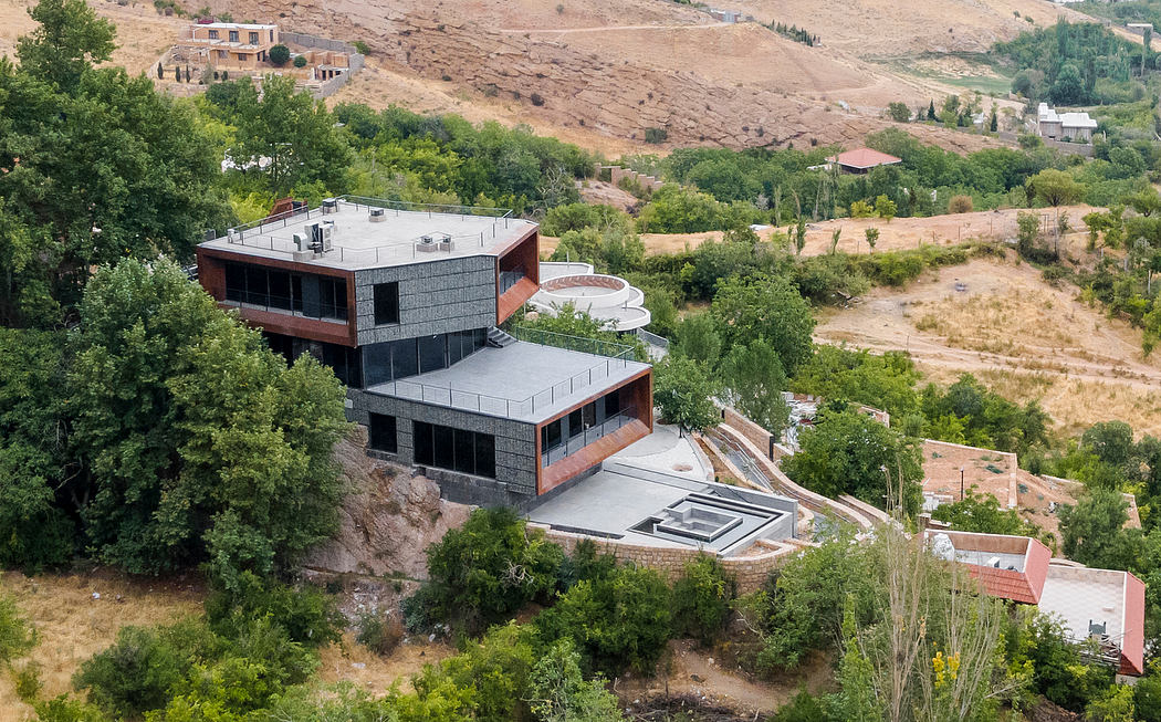 A modern, multi-level structure perched on a hillside, featuring a geometric design and large windows.