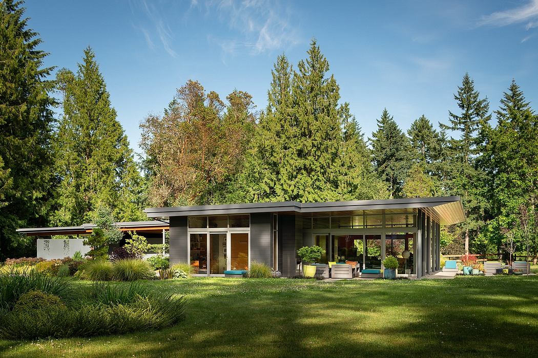 Modern single-story house with floor-to-ceiling windows, surrounded by lush greenery.