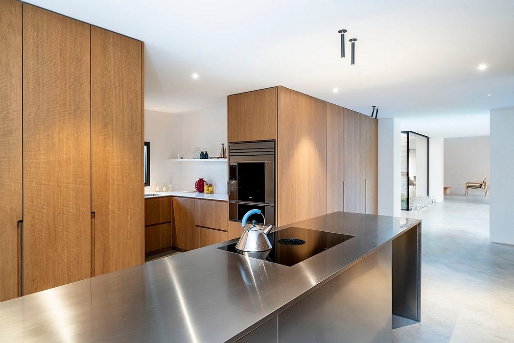 Modern, minimalist kitchen with sleek stainless steel countertops, wood cabinetry, and recessed lighting.