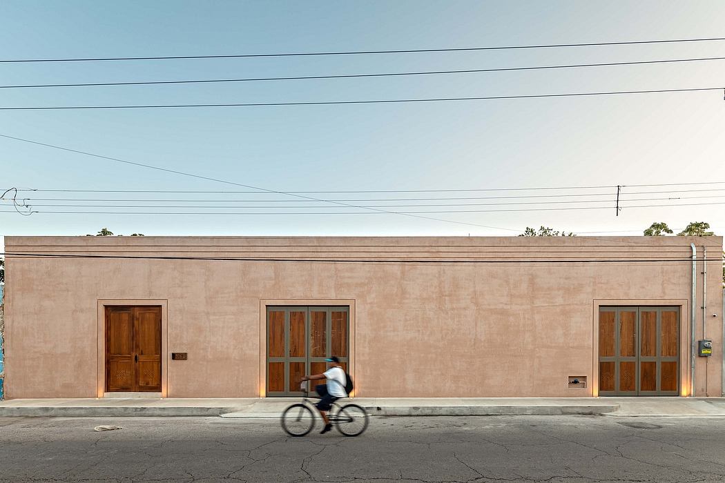 A tan stucco building with wooden doors and windows, a person riding a bicycle in the foreground.