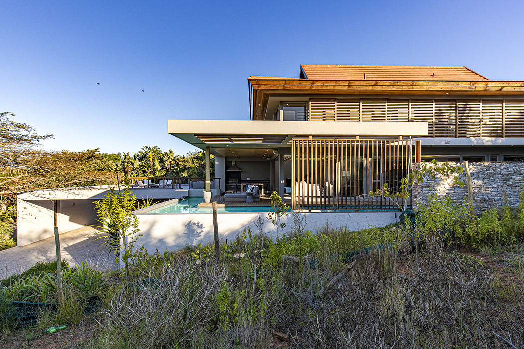 Sprawling modern home with wooden beams, stone accents, and a pool overlooking lush greenery.