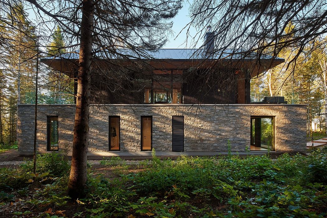 A modern, stone-clad cabin nestled among lush foliage, featuring a unique roof design.