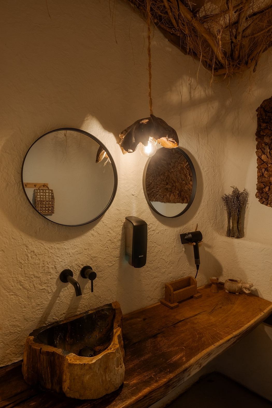 Rustic bathroom with oval mirrors, wooden vanity, and artistic lighting fixture.