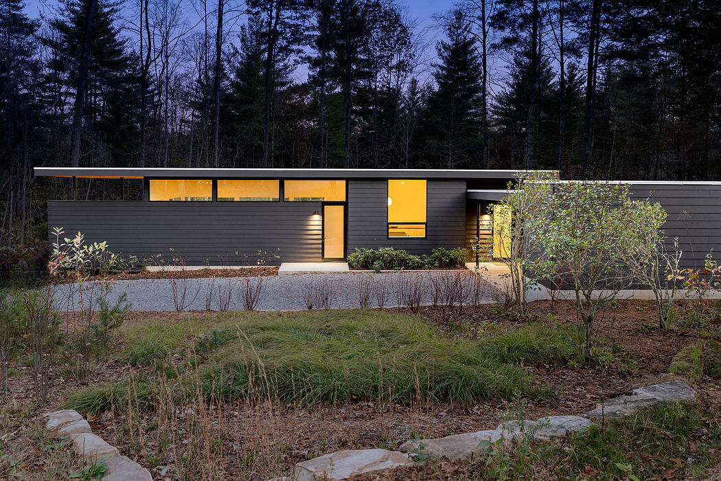 A modern, single-story home with clean lines, large windows, and a dark exterior surrounded by trees.