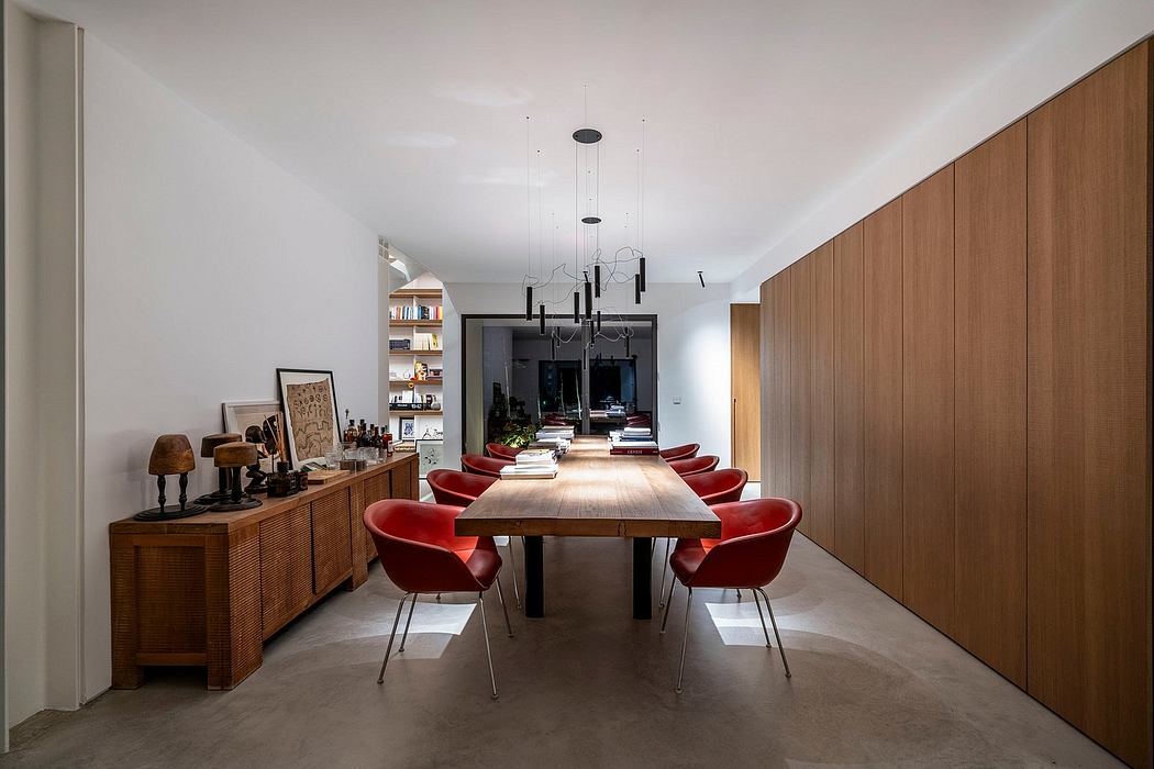 A modern dining room with a wood table, red chairs, and built-in wall shelving.