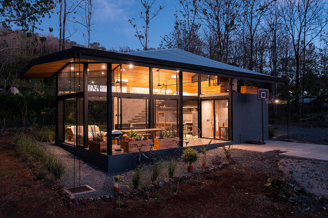 A modern, glass-walled cabin nestled in a wooded setting, with warm interior lighting.
