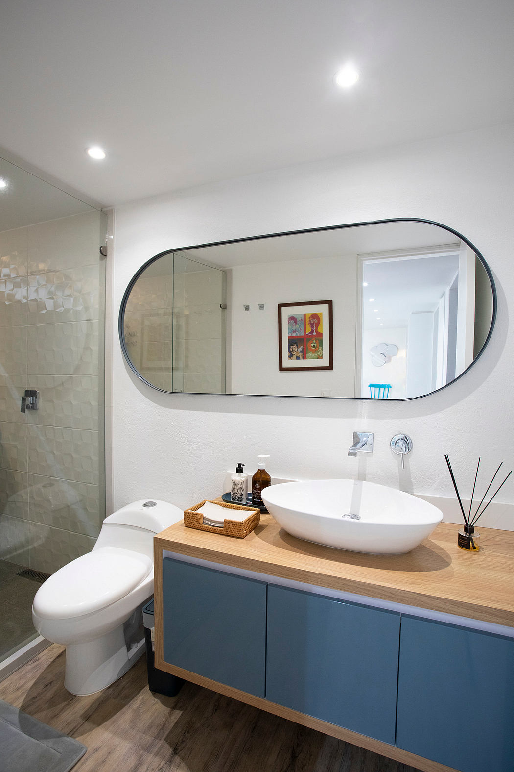 Stylish bathroom with modern vanity, oval mirror, and accent art framed on wall.