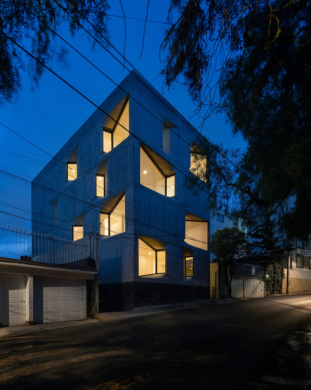 A modern residential building with an angular, geometric facade illuminated at night.