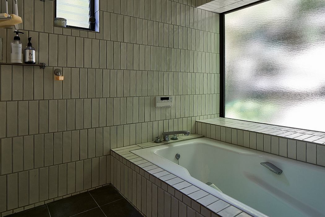 A modern bathroom with rectangular tiles, a large bathtub, and a window offering a view.