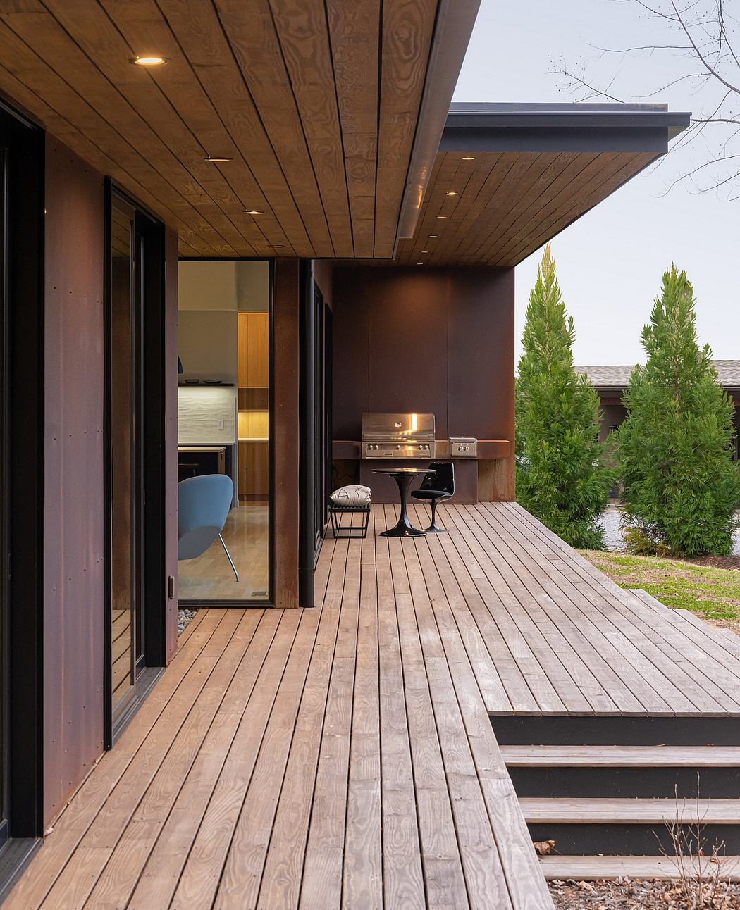 Modern wooden deck with built-in grill, patio furniture, and glass doors leading inside.