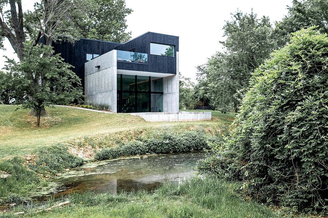 A modern, minimalist home nestled in a lush, forested landscape with a small pond.