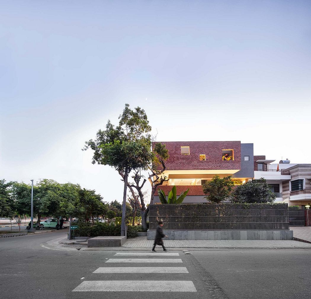 A modern brick building with large windows and balconies surrounded by trees and a crosswalk.