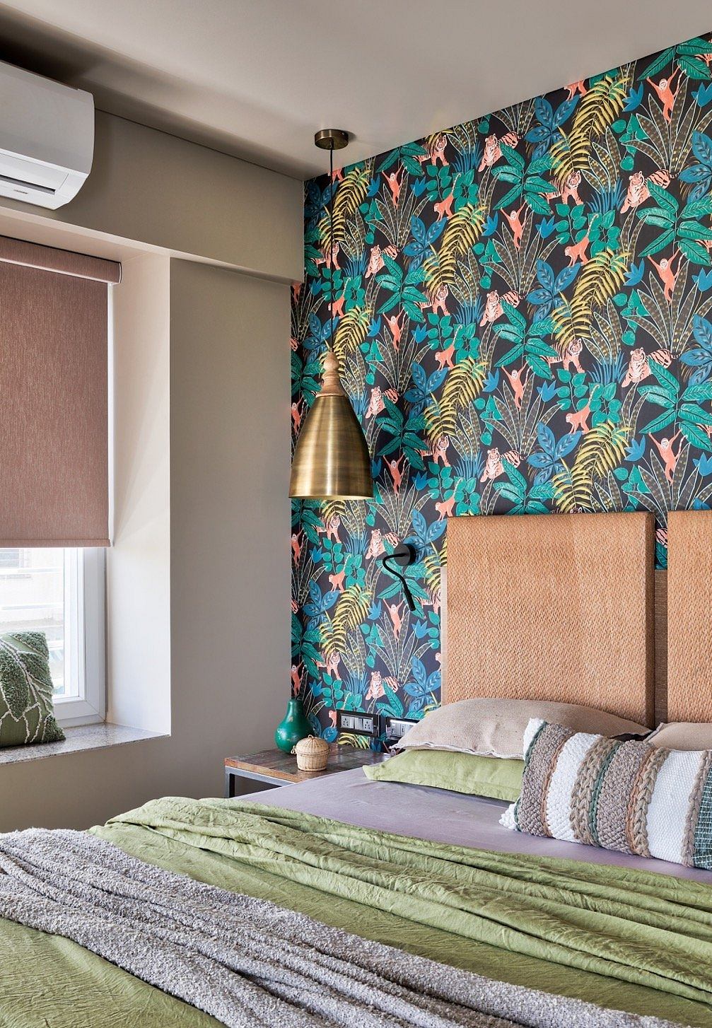 Lush tropical wallpaper, brass pendant, and textured bedding in a cozy bedroom design.