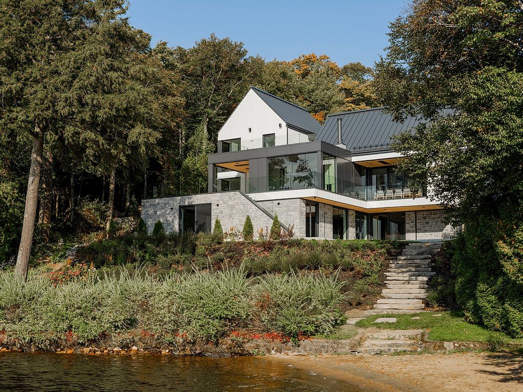 A modern home with a complex roofline, glass walls, and a stone foundation along a river.