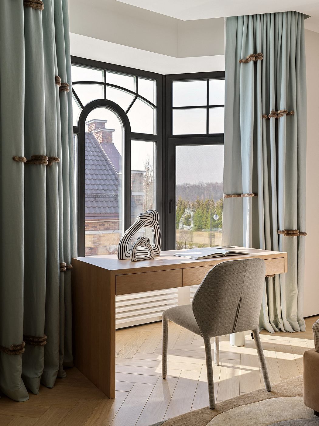 A modern, cozy workspace with large arched windows, wooden desk, and textured curtains.