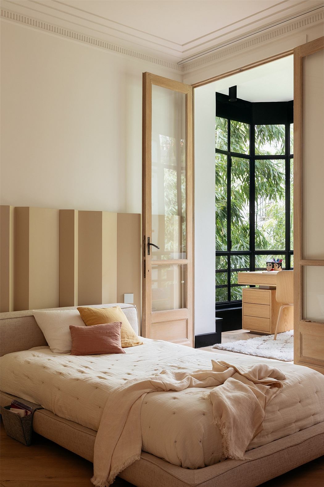 Elegant bedroom with tall windows, wood accents, and a cozy bed overlooking greenery.