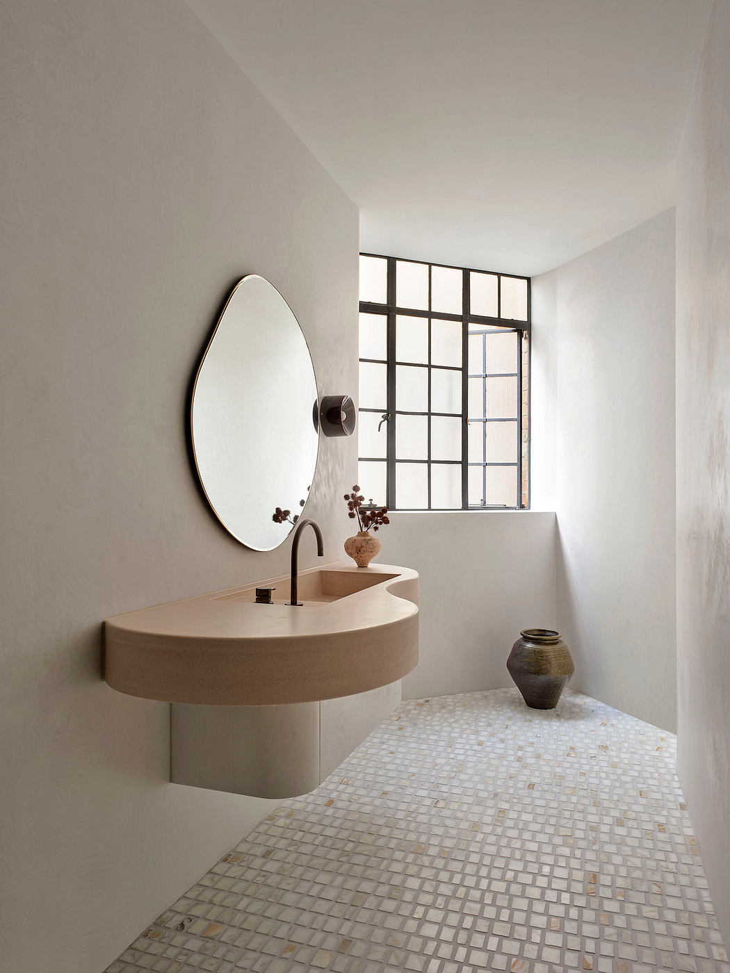 Minimalist bathroom design with curved vanity, round mirror, and mosaic tile floor.