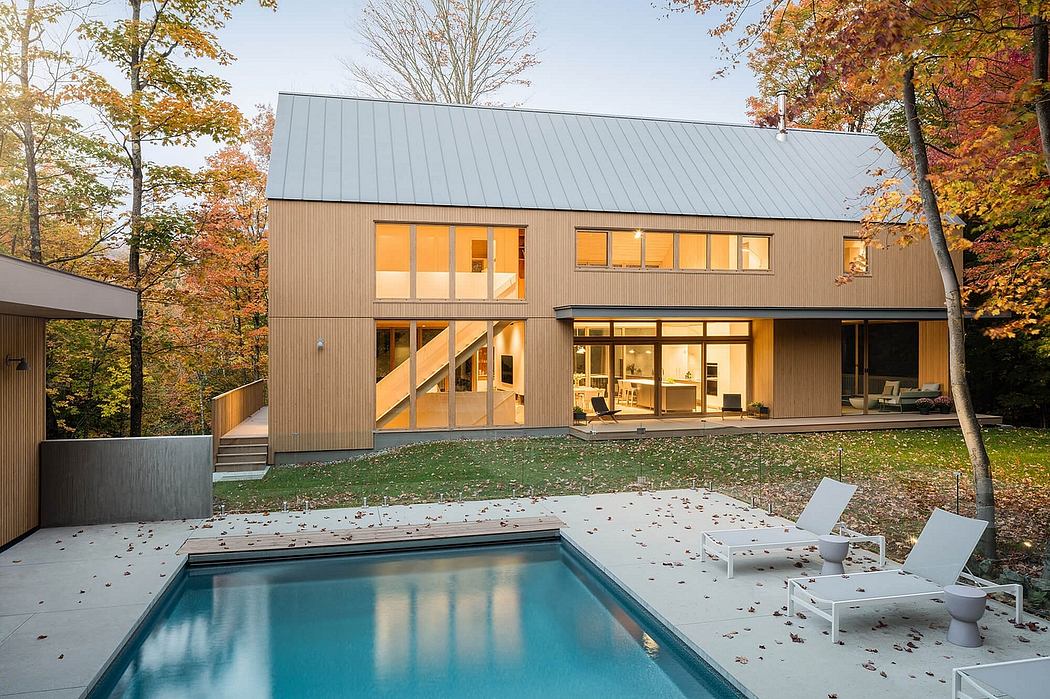 A modern two-story home with a flat metal roof, large windows, and a swimming pool surrounded by autumn foliage.