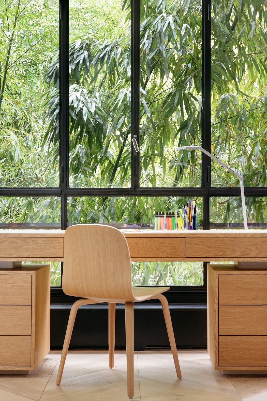 A modern, minimalist home office with large windows overlooking lush greenery.
