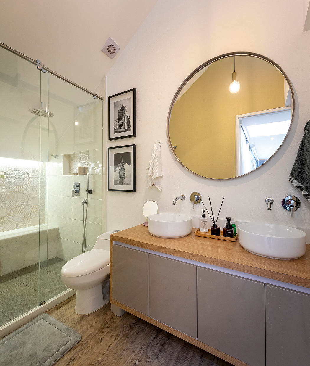 Modern bathroom with round mirror, vanity, and glass shower enclosure.