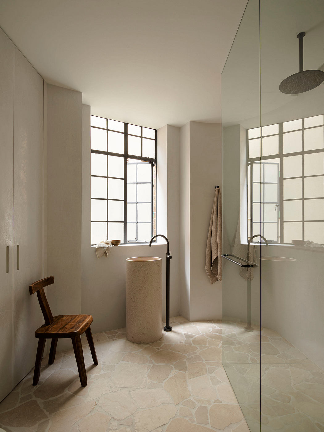 Minimalist bathroom with large windows, stone floor, and wooden furnishings.