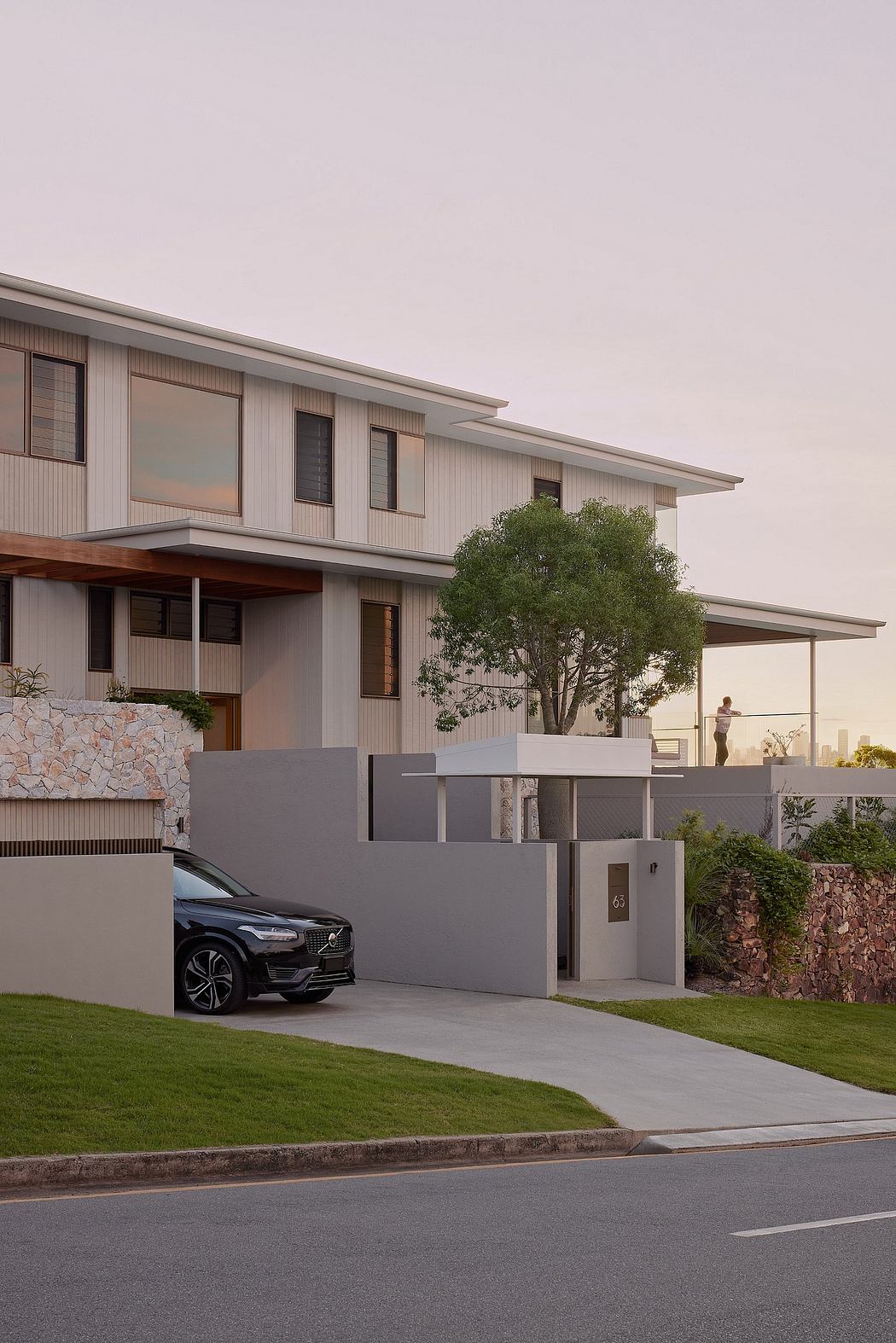 Modern two-story home with sleek exterior, large windows, and covered entryway. Volvo SUV parked in driveway.