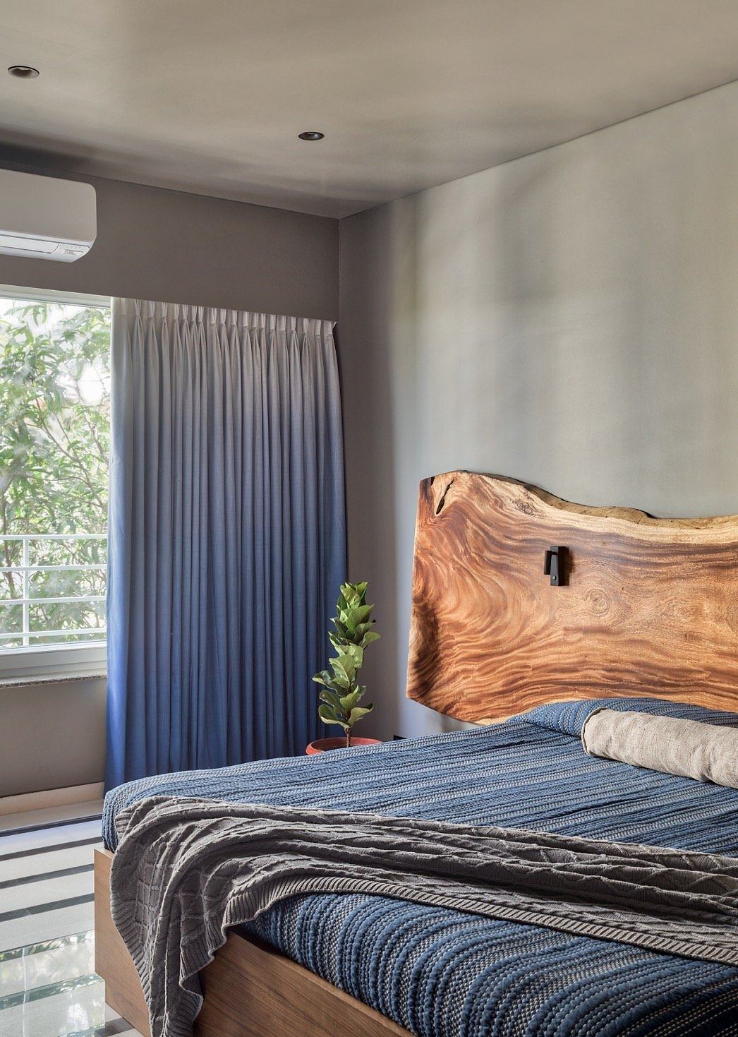 Wooden headboard, gray curtains, and striped bedding create a cozy, modern bedroom.