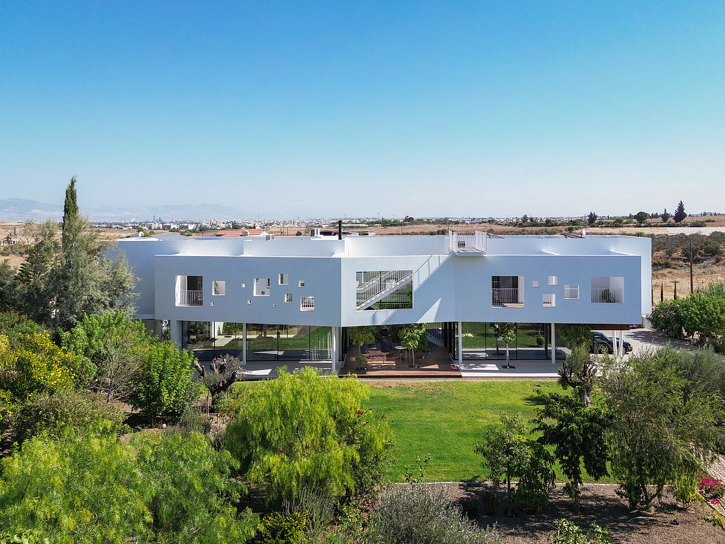 Modern white apartment building with balconies overlooking a lush green garden landscape.