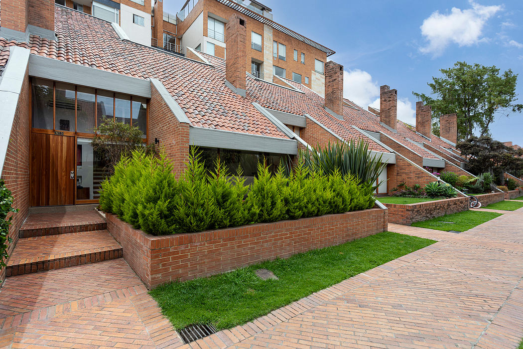 Brick apartment building with terracotta tiled roofs, lush landscaping, and brick walkway.