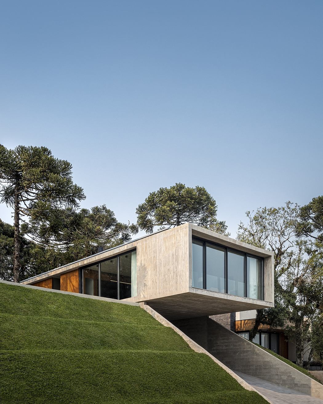 Modern house with wood, glass, and concrete elements, surrounded by lush greenery.