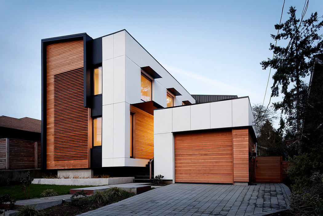 Modern house with wooden and concrete exterior panels, large windows, and a paved driveway.