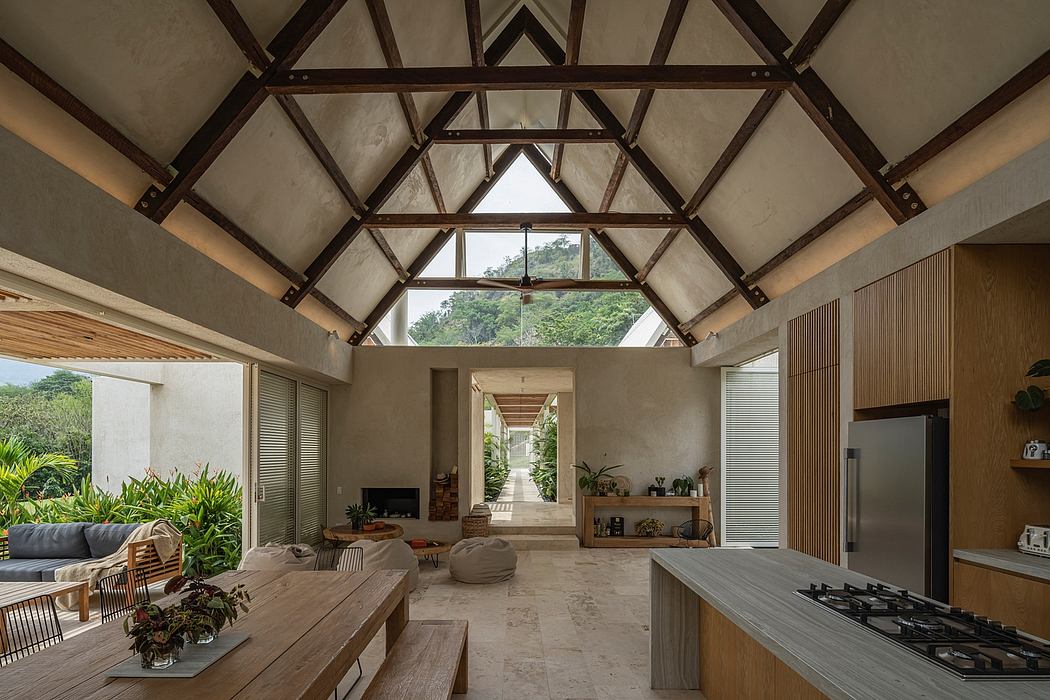 Expansive open-concept living space with vaulted wooden truss ceiling and lush greenery view.