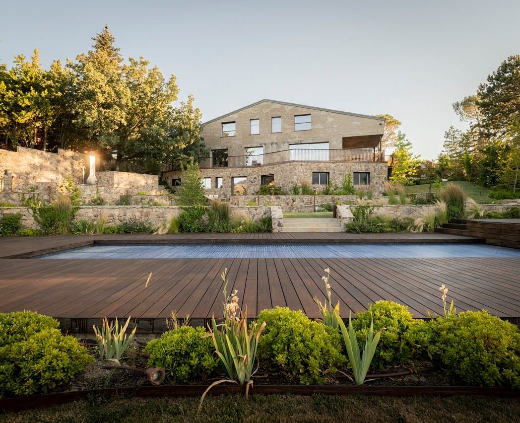 Stately modern multi-level residence with stone facade and expansive wooden deck overlooking lush landscaping.