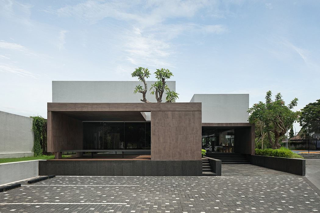 Modern, minimalist exterior with stone and glass facade, lush greenery, and paved entrance.