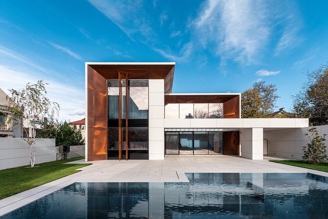 A modern, two-story home with clean lines, glass walls, and a reflecting pool in the foreground.