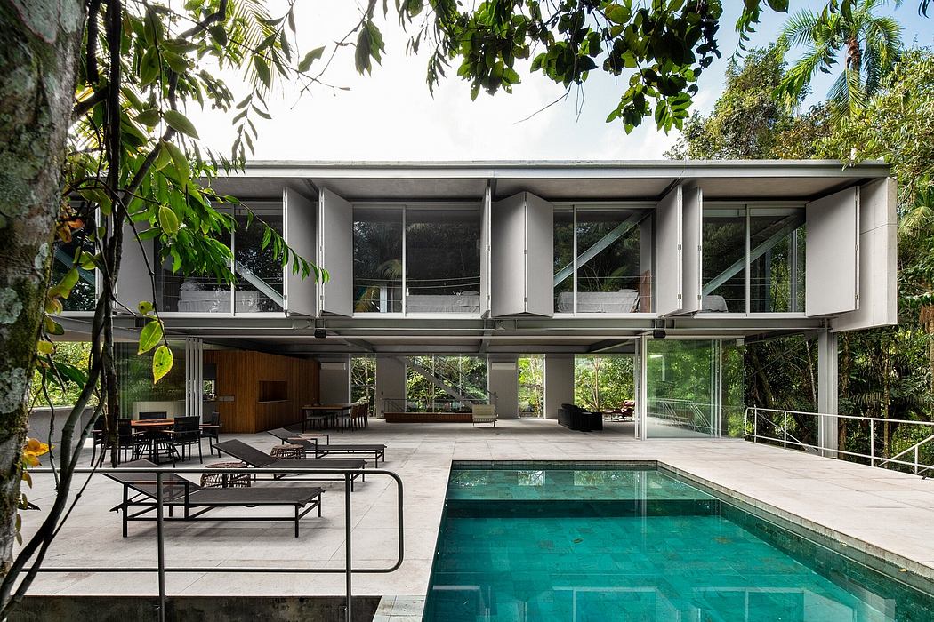 A modern, glass-walled house with a swimming pool surrounded by lush greenery.