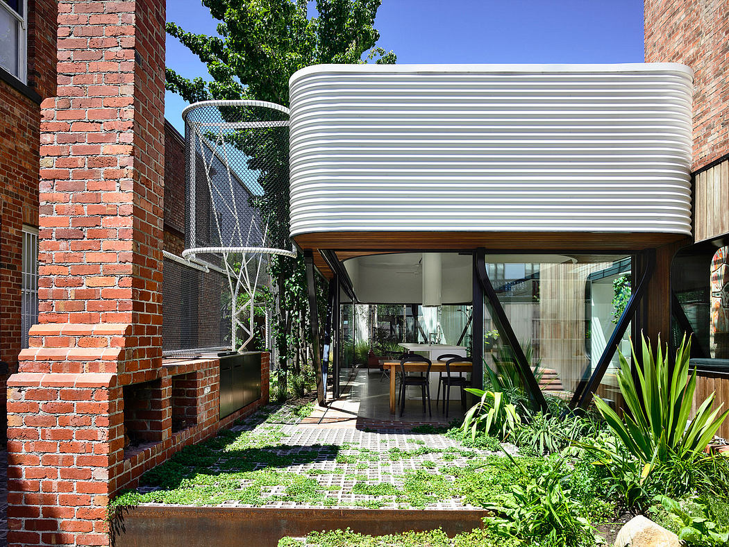 A modern outdoor patio with a curved, corrugated metal roof structure and lush greenery.