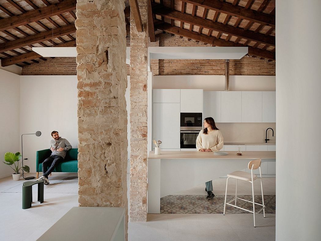 A modern, open-concept kitchen with exposed brick walls, wooden ceiling beams, and sleek white cabinetry.