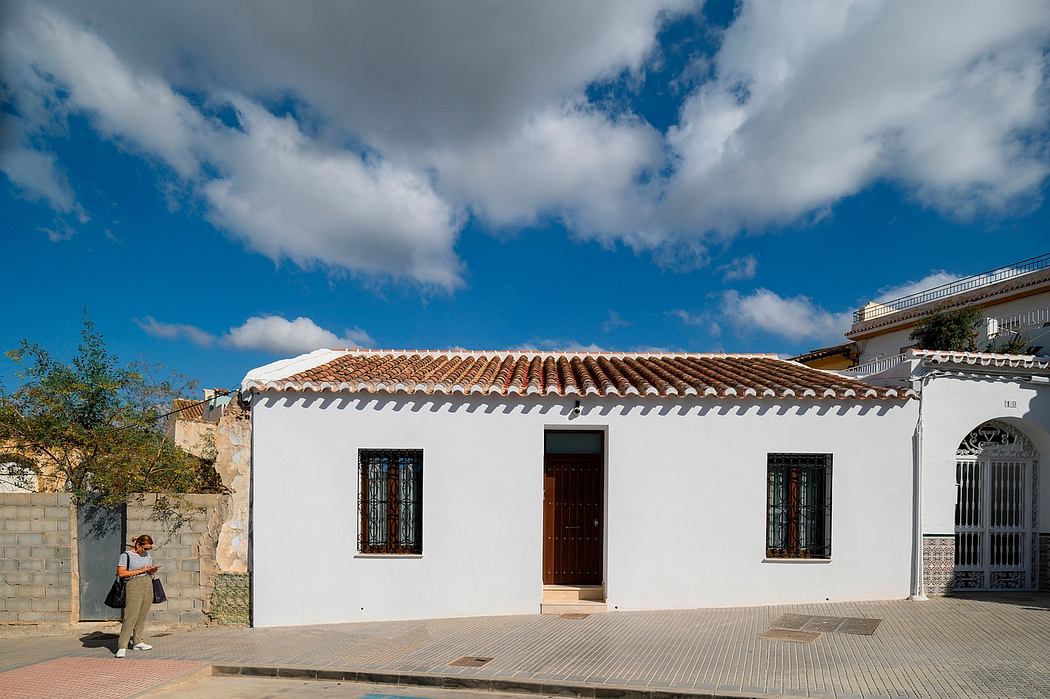 A traditional Spanish-style white building with a tiled roof, wrought-iron windows, and a wooden door.