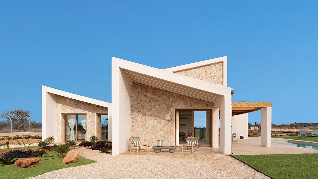 A modern, stone-clad villa with symmetrical entryways and a covered patio, set against a blue sky.