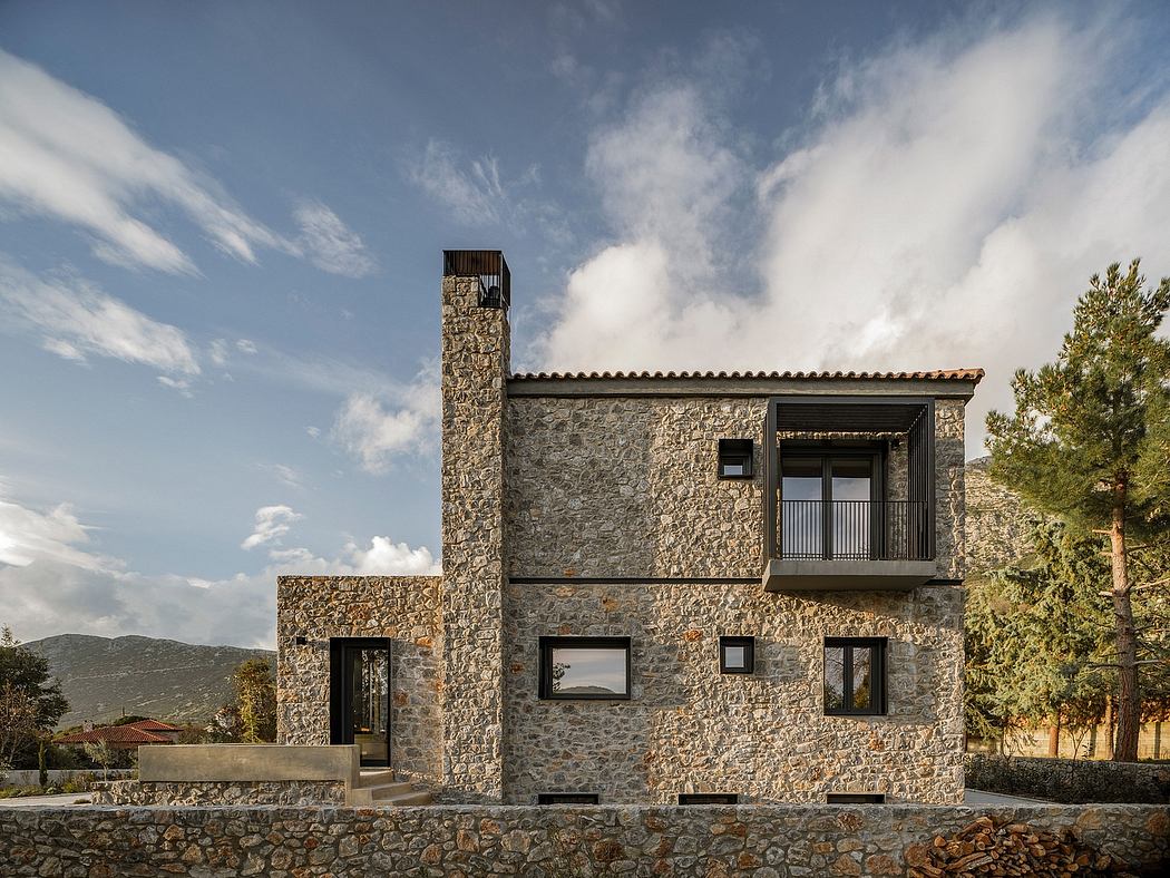 A rustic stone house with a balcony, large windows, and a stone chimney against a cloudy sky.