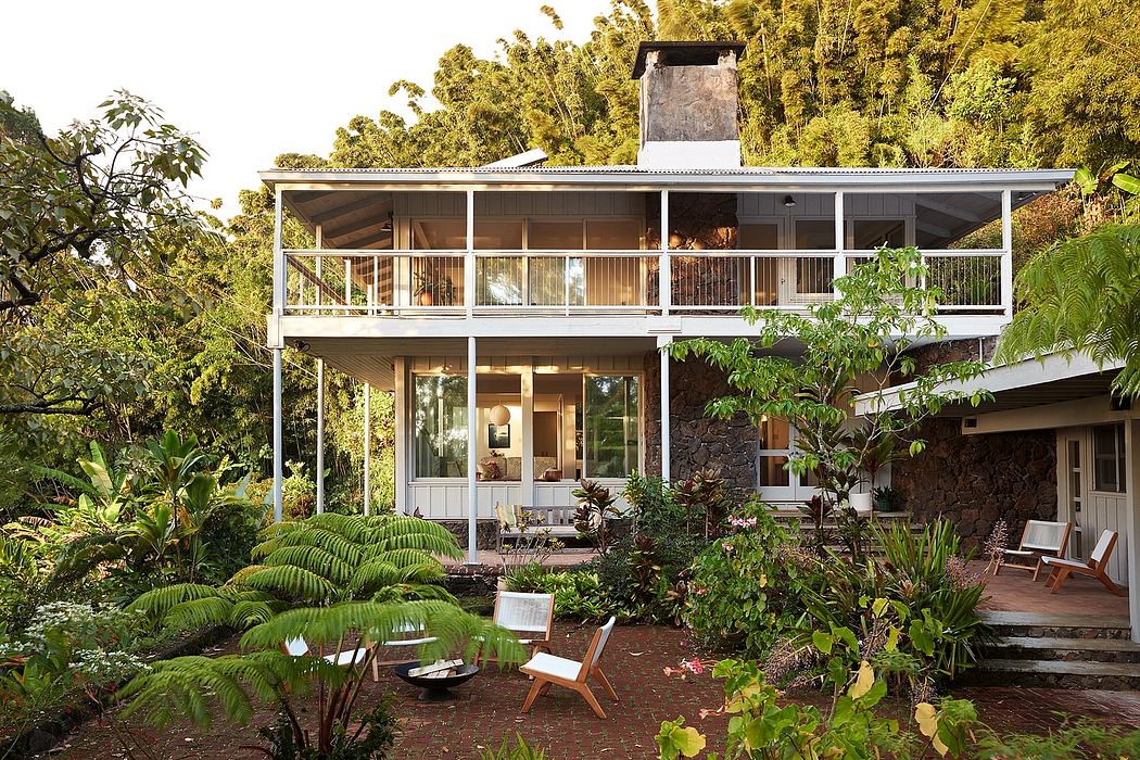 A two-story tropical retreat with a covered deck, surrounded by lush greenery.