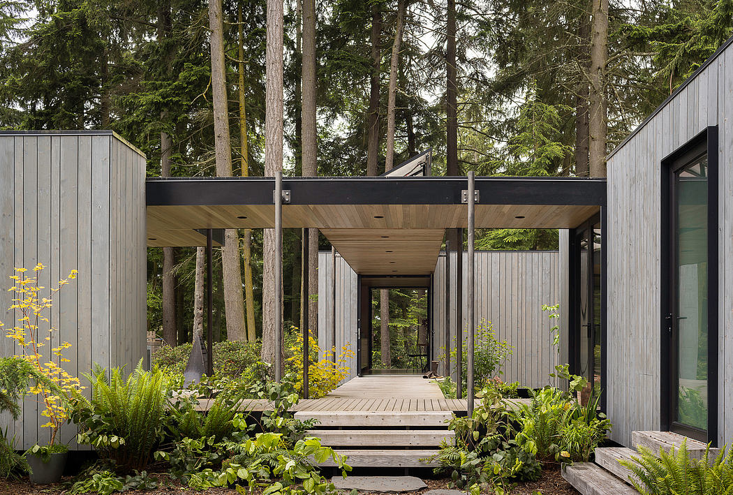 A modern, wooden cabin surrounded by lush forest, with a covered walkway and glass façade.