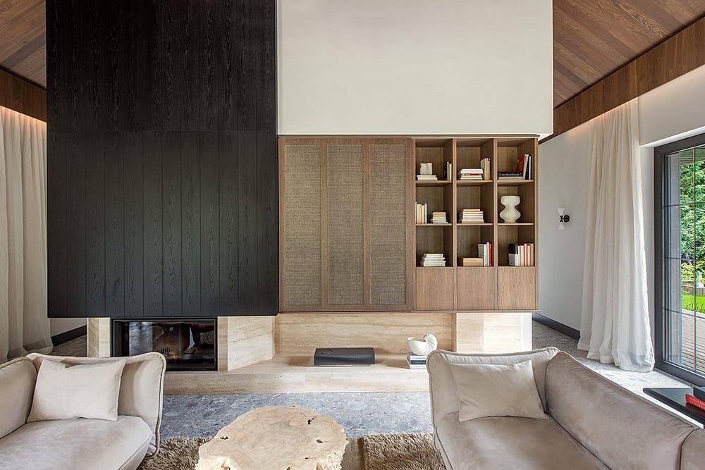 Minimalist living room with dark wood paneling, built-in bookshelves, and large fireplace.