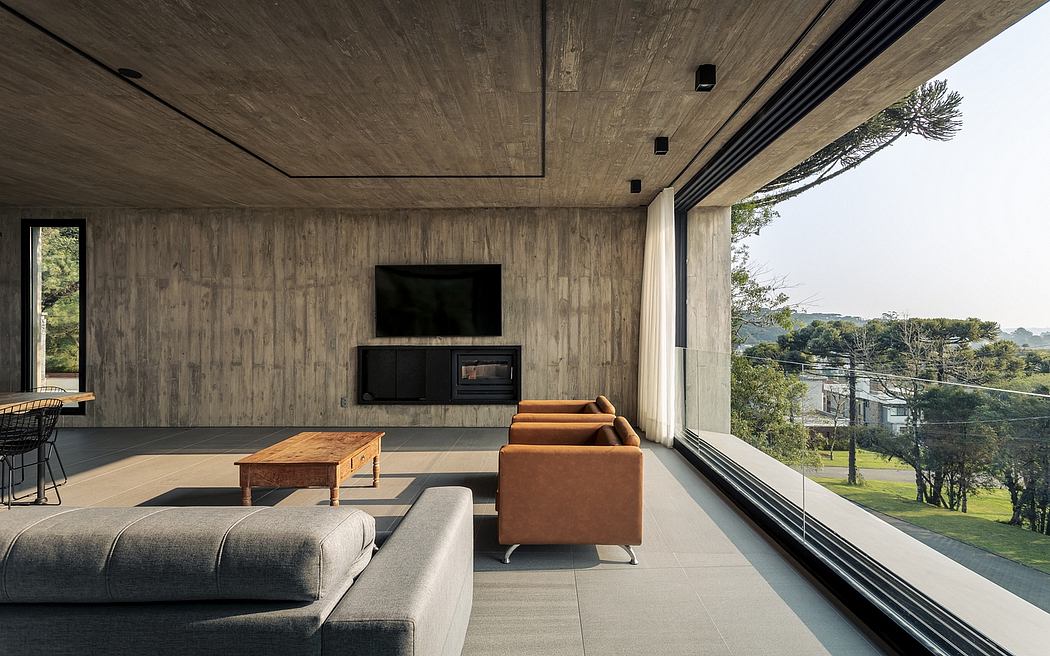 A modern living room with concrete walls, large windows overlooking nature, and a mix of gray and orange furniture.