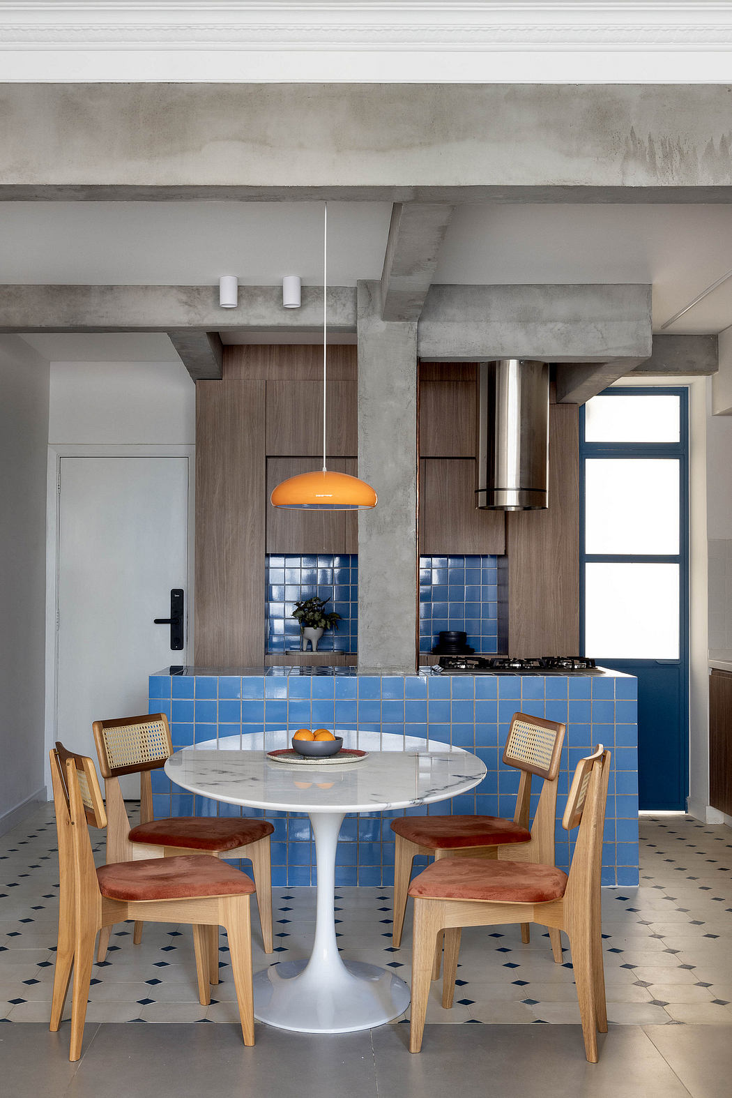 Modern kitchen with concrete beams, blue tile backsplash, round marble table, and wooden chairs.