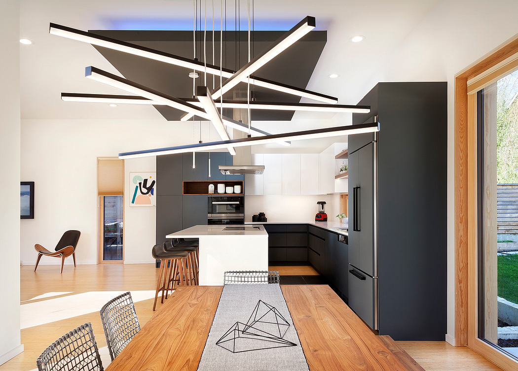 Modern, open-plan kitchen with sleek black cabinetry, geometric lighting fixture, and wooden dining table.