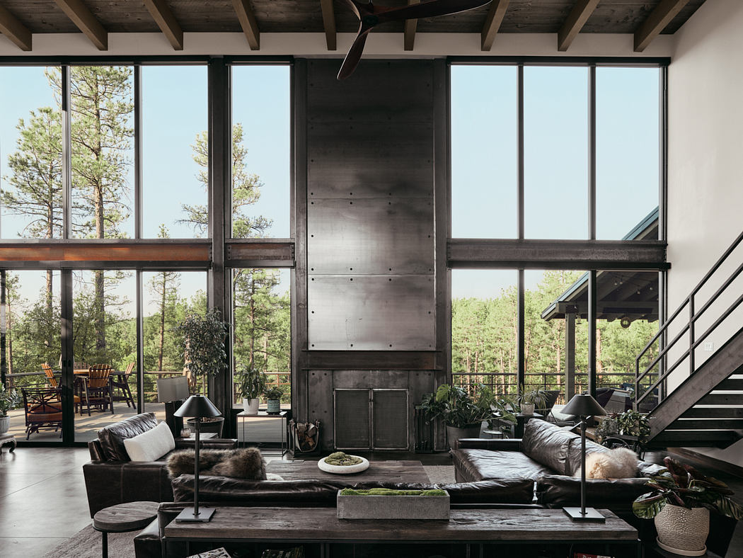 Open-concept living room with wooden beams, large windows, and a modern industrial fireplace.