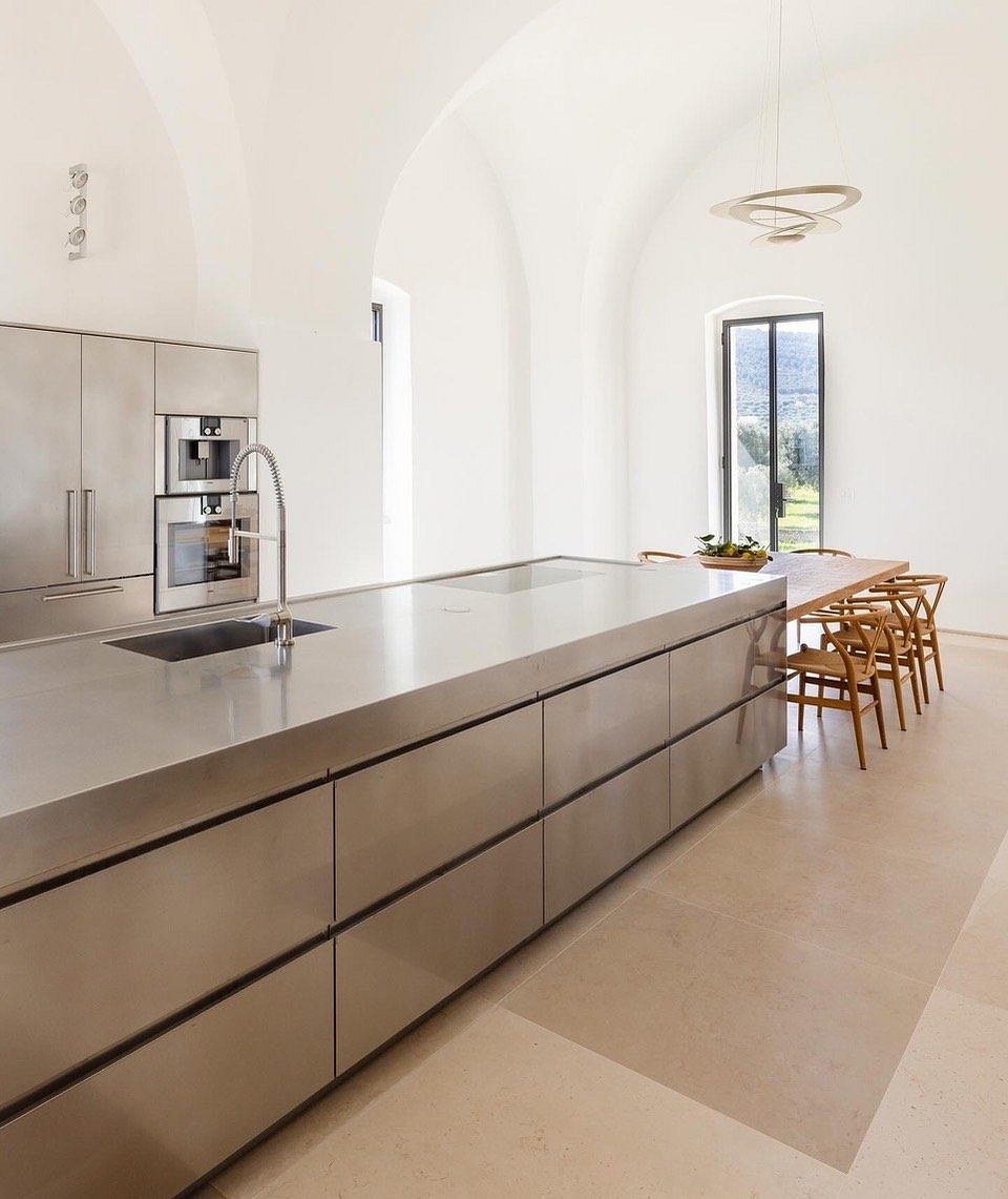 Minimalist kitchen with sleek stainless steel cabinetry, arched windows, and modern lighting.
