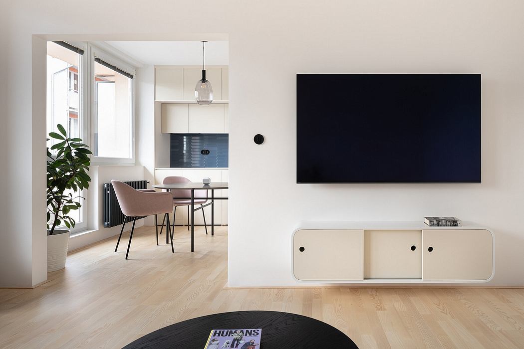 Minimalist living space with a large TV, sleek white furniture, and wood flooring.